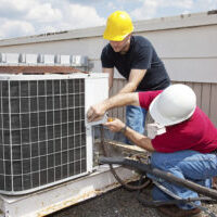 Two workers on the roof of a building working on the air conditioning unit.